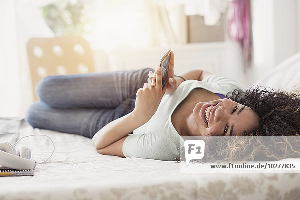 Porträt eines Mädchens im Teenageralter (16-17)  das im Schlafzimmer SMS schreibt