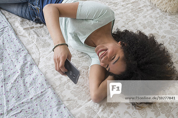 Teenager-Mädchen (16-17)  das im Schlafzimmer SMS schreibt