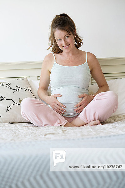 Smiling pregnant woman sitting on bed