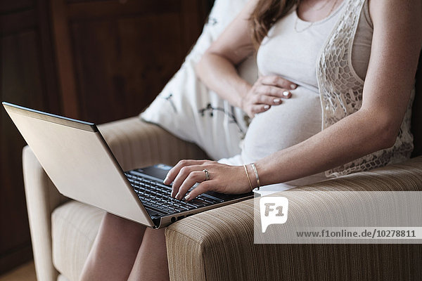 Mid-section of pregnant woman using laptop