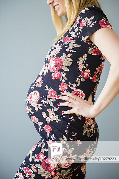 Studioaufnahme einer schwangeren Frau im geblümten Kleid