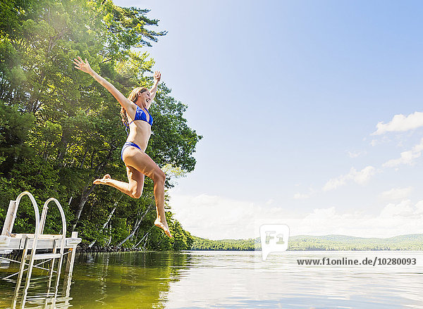 Young woman jumping into lake from jetty