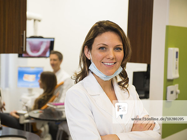 Porträt eines Zahnarztes mit einem Kollegen und einem Patienten im Hintergrund