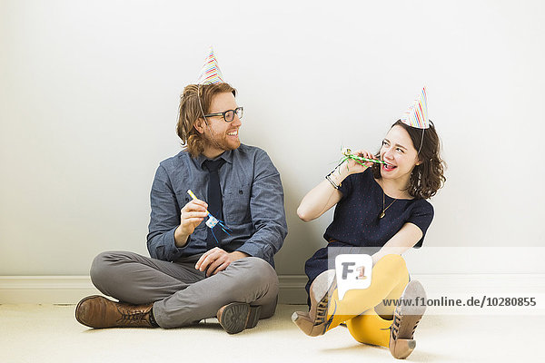 Ehepaar mit Partyhornbläsern und Partyhüten auf dem Boden sitzend