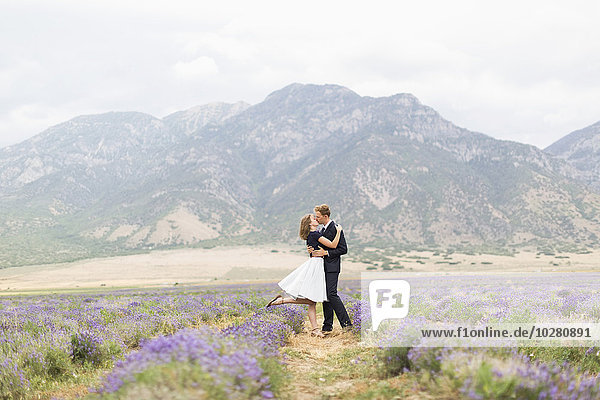 Neuvermähltes Paar  das sich in einem Lavendelfeld mit Bergen im Hintergrund küsst