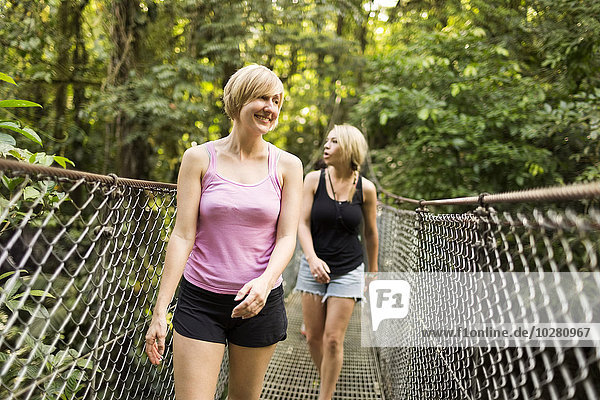 Young women walking on footbridge in forest