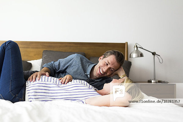 Ehemann auf dem Bett liegend mit schwangerer Frau