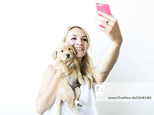 Studio shot of woman photographing self with Golden Retriever puppy
