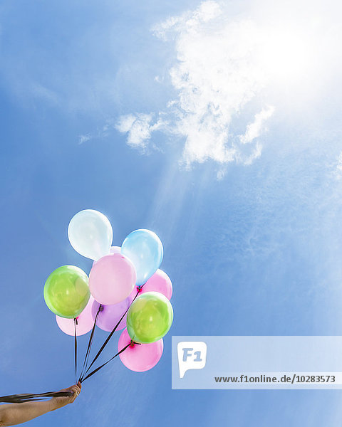 Hand holding balloons against blue sky