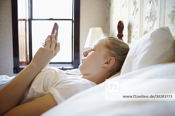 Young woman in bed with cell phone