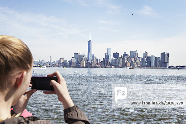 Junge Frau  die mit ihrem Smartphone ein Foto von Manhattan macht