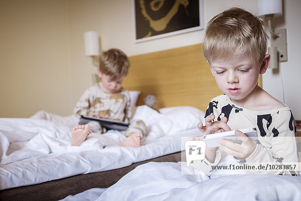 Jungen im Schlafzimmer spielen mit digitalen Geräten