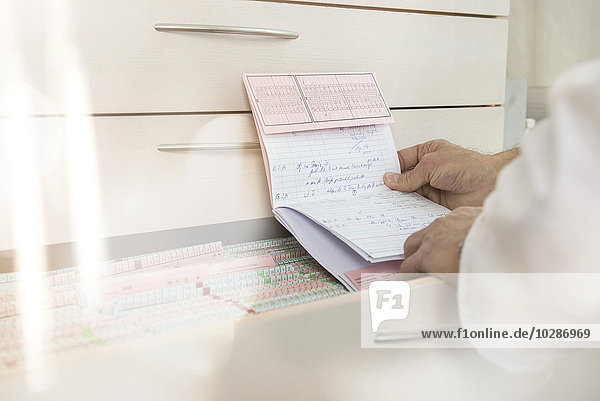 Männlicher Arzt,  der die Karteikarte eines Patienten mit Schubladen liest,  München,  Bayern,  Deutschland
