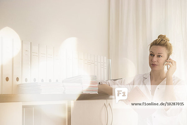 Female doctor holding a medical record and talking on a mobile phone  Munich  Bavaria  Germany