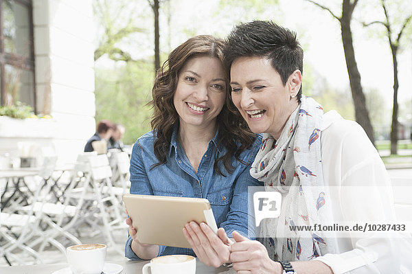 Zwei Freunde benutzen ein digitales Tablet in einem Straßencafé  Bayern  Deutschland