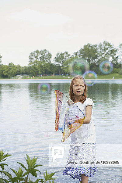 Girl catching soap bubbles with fishing net in the lake  Bavaria  Germany