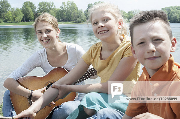 Young leader playing guitar with her friends at lakeside  Bavaria  Germany