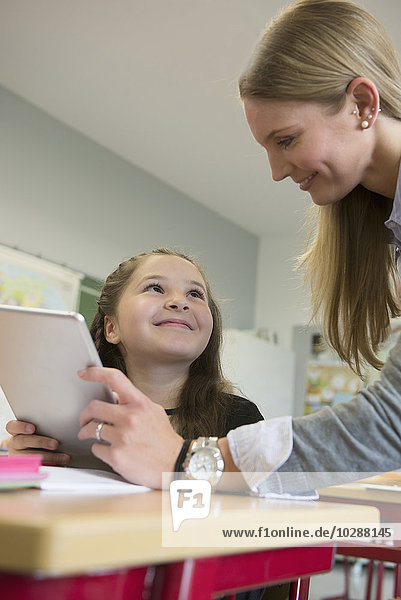 Lehrerin zeigt einem Mädchen etwas auf einem digitalen Tablet-PC im Klassenzimmer  München  Bayern  Deutschland