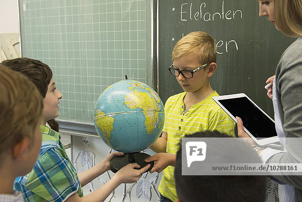 Lehrerin und Schüler betrachten einen Globus im Klassenzimmer  München  Bayern  Deutschland