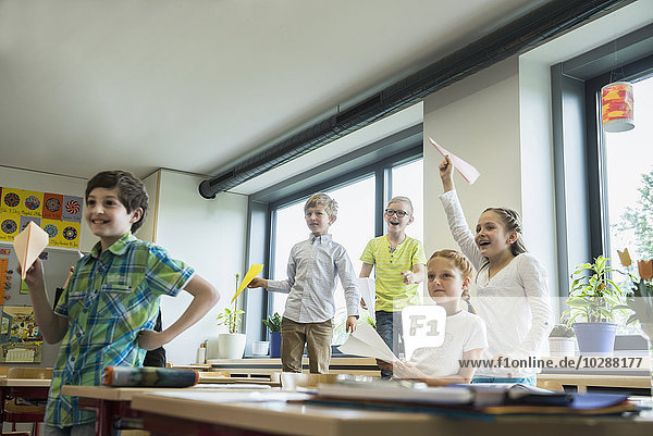 Schulkinder spielen mit Papierfliegern im Klassenzimmer  München  Bayern  Deutschland