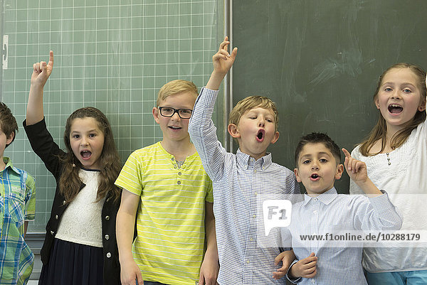 Schüler heben die Hände vor der Tafel in einem Klassenzimmer  München  Bayern  Deutschland