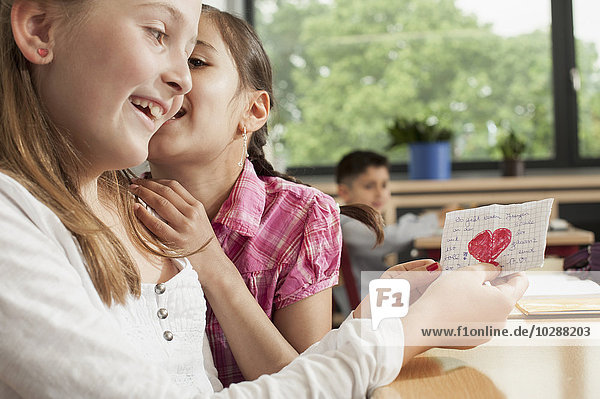 Schulmädchen flüstern im Klassenzimmer und zeigen einen Liebesbrief  München  Bayern  Deutschland