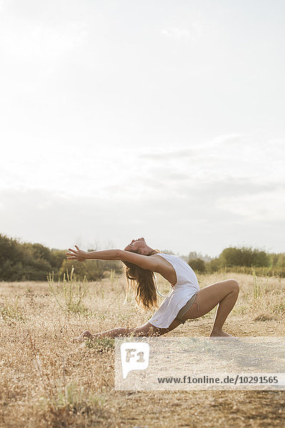 Boho Frau in Hochsichel-Longe-Yoga-Pose im sonnigen ländlichen Feld
