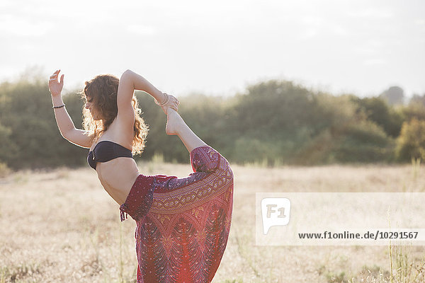 Boho Frau in König Tänzerin Yoga Pose im sonnigen ländlichen Bereich