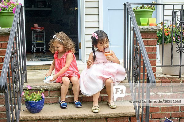 Zwei junge Mädchen  die auf Stufen sitzen und Eis am Stiel essen