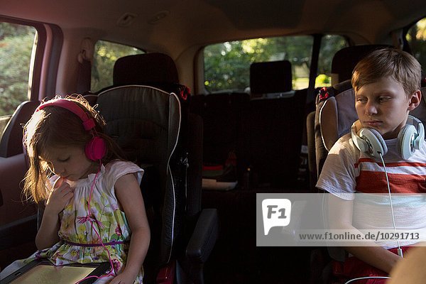 Junge beobachtet jüngere Schwester mit digitalem Tablett auf dem Rücksitz im Auto