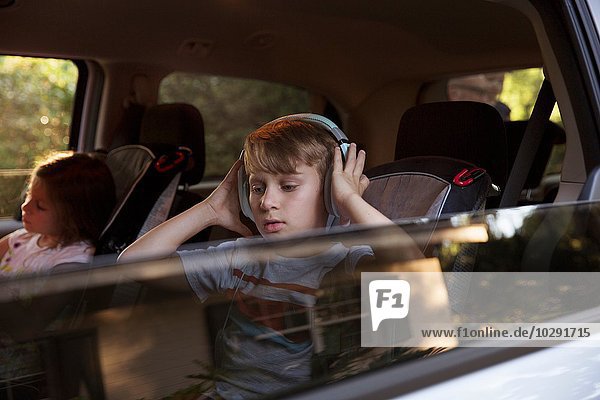 Junge mit jüngerer Schwester  die auf dem Rücksitz des Autos Kopfhörer hört.