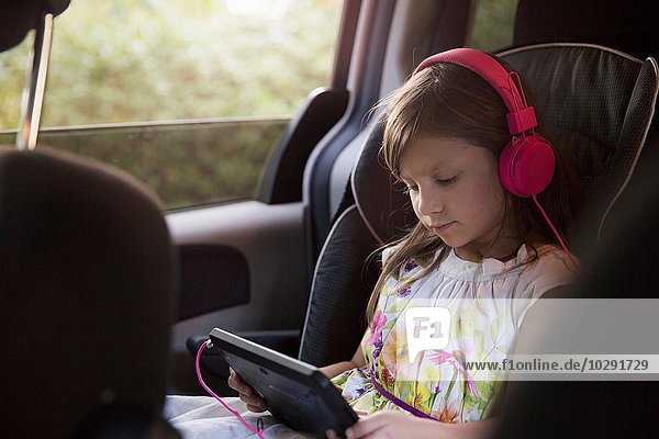 Mädchen mit rosa Kopfhörer mit digitalem Tablett im Auto