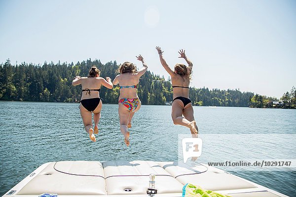 Rear view of three young women jumping from pier  Lake Oswego  Oregon  USA