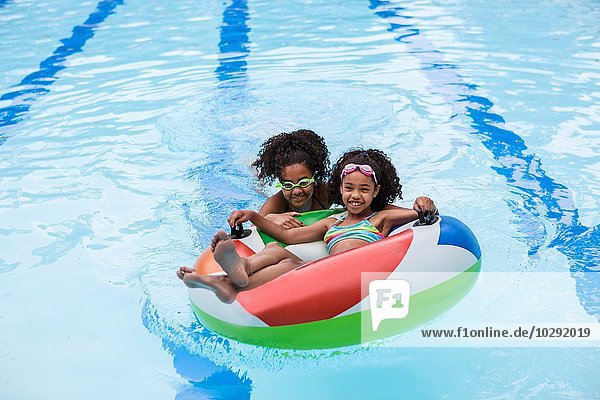 Girls in swimming pool playing with inflatable ring  looking at camera smiling