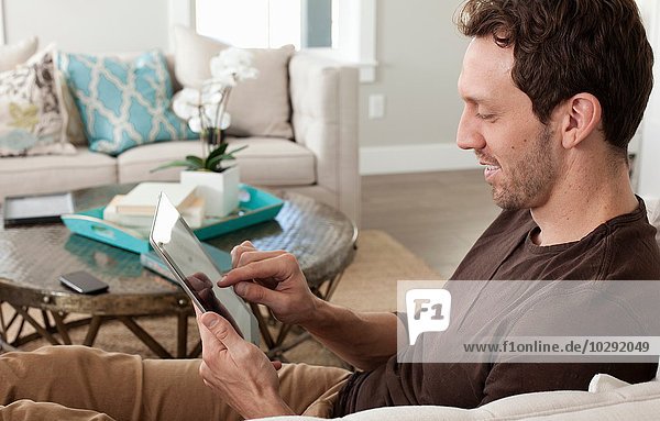 Mittlerer Erwachsener Mann  der sich zu Hause entspannt  mit Hilfe eines digitalen Tabletts.