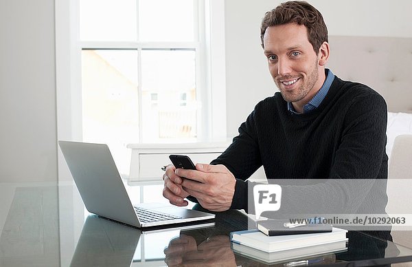 Mid adult man sitting at table  using laptop and smartphone