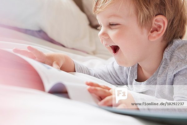 Head and shoulders of boy on bed lying on front looking at storybook  laughing