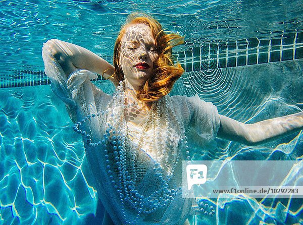 Junge Frau unter Wasser  trägt ein dünnes weißes Hemd und Perlen.