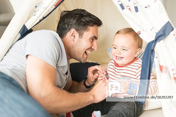 Vater und Sohn sitzen im Spielzelt im Haus und lachen gemeinsam.