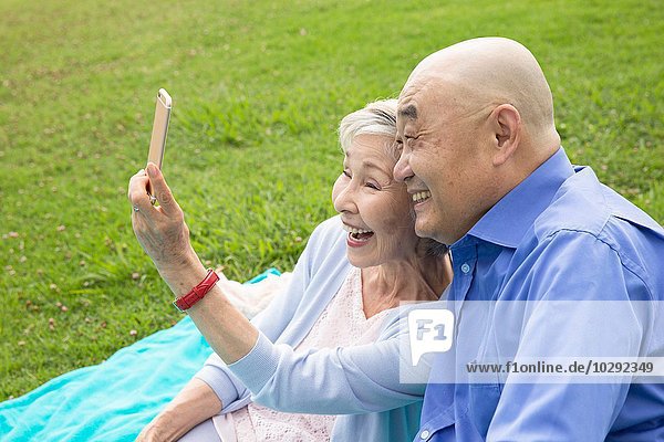 Seniorenpaar im Park sitzend  Selbstporträt mit dem Smartphone aufnehmend
