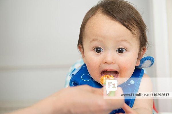 Hand of mother feeding baby food to open mouthed son in kitchen