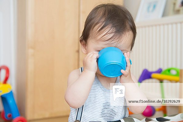Baby boy drinking from baby cup in playroom