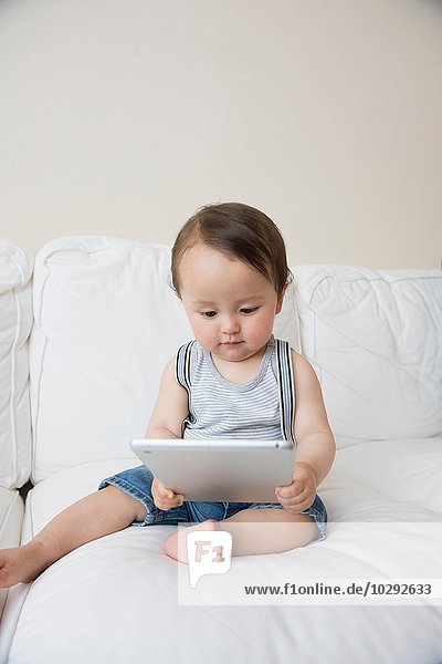 Baby boy sitting on sofa looking at digital tablet