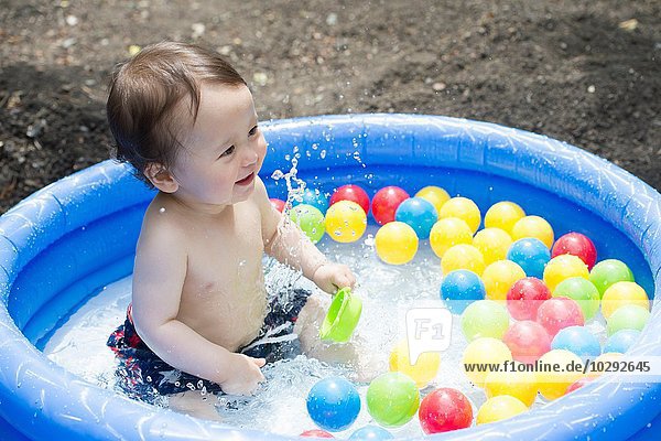 Baby boy splashing in garden paddling pool