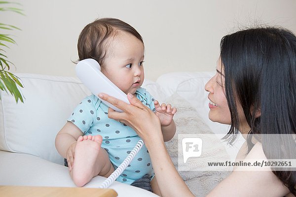 Baby Junge und Mutter hören Festnetztelefon auf Sofa