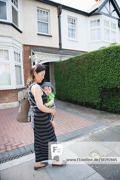 Mature mother and son in baby sling strolling along street