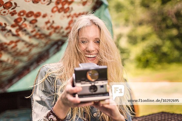 Porträt einer jungen Frau beim Fotografieren mit Sofortbildkamera beim Zelten