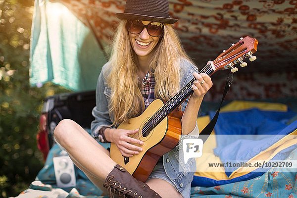 Porträt einer jungen Frau die beim Zelten im Stiefel die Ukulelele spielt.