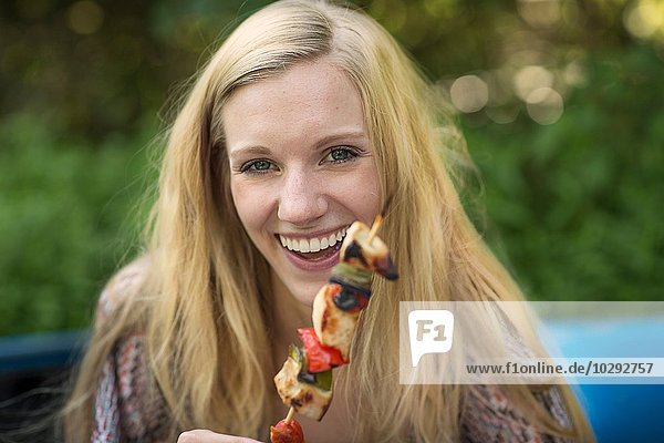 Portrait of young woman holding barbecued kebab stick
