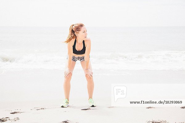 Mittlere erwachsene Frau am Strand stehend  Hände auf Knien  wegschauend